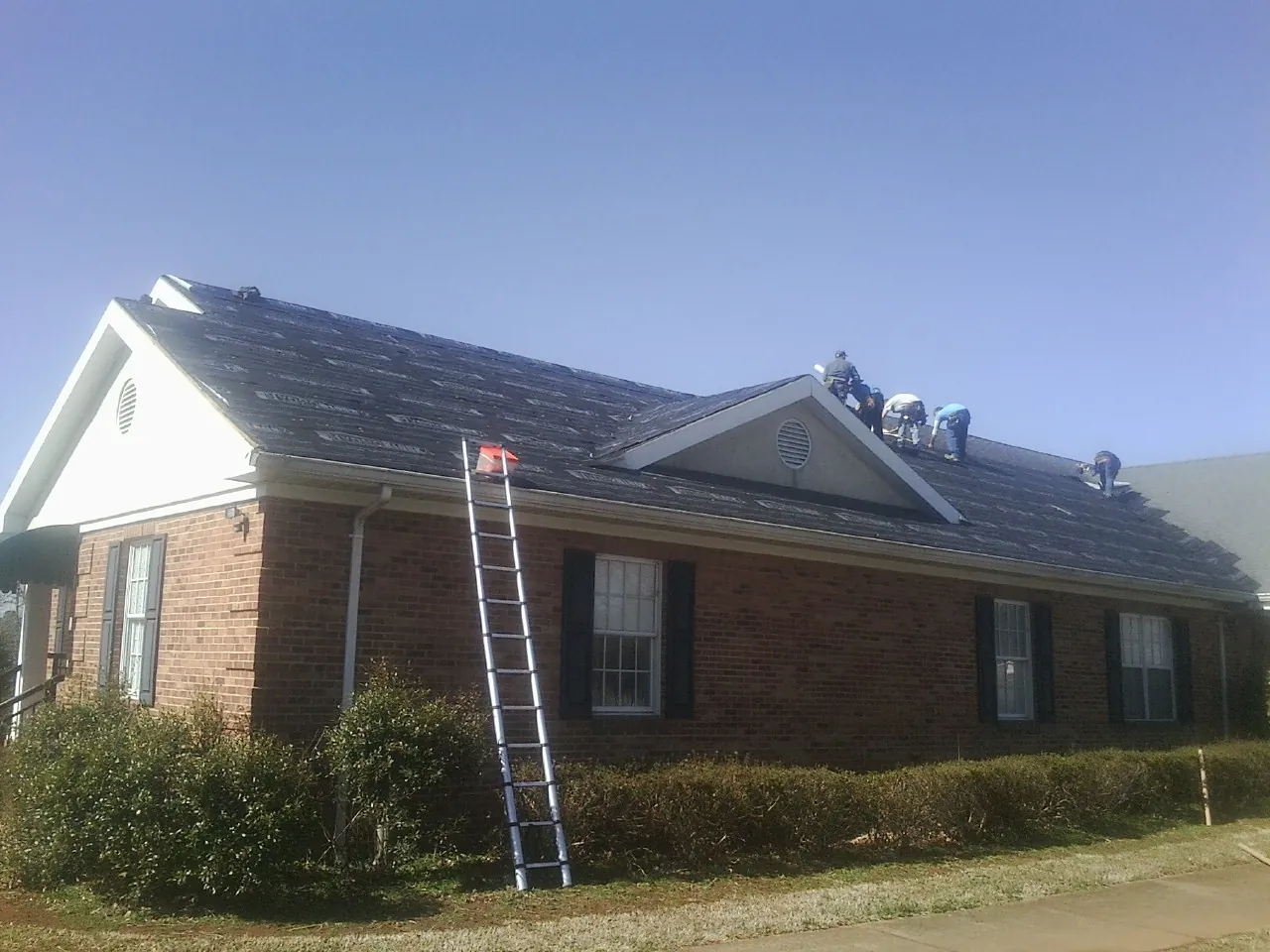 Crew tearing shingles off a brick ranch roof with a ladder set — Metal Roof Repair work by our crew in Hubbardsville