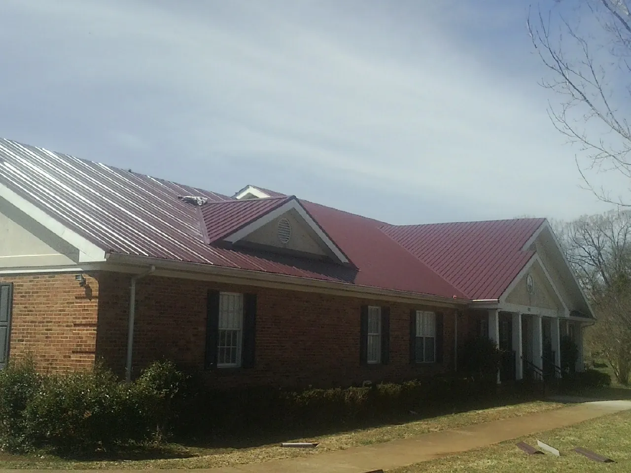 Red metal roof with gabled entries on a long brick building, from a Hail Damage Roof Repair job in Hubbardsville