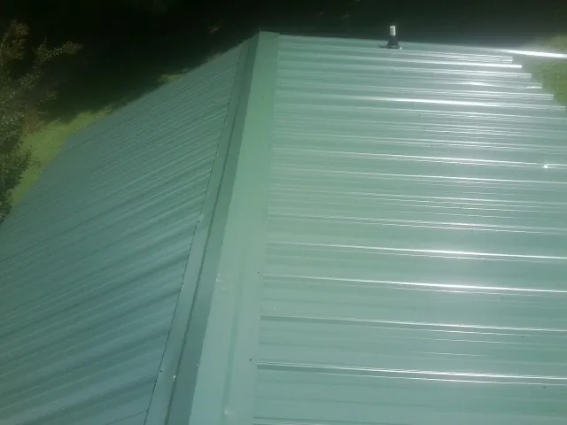 New green metal panels meeting at the ridge of a roof — Flat Roof Repair work by our crew in Hubbardsville