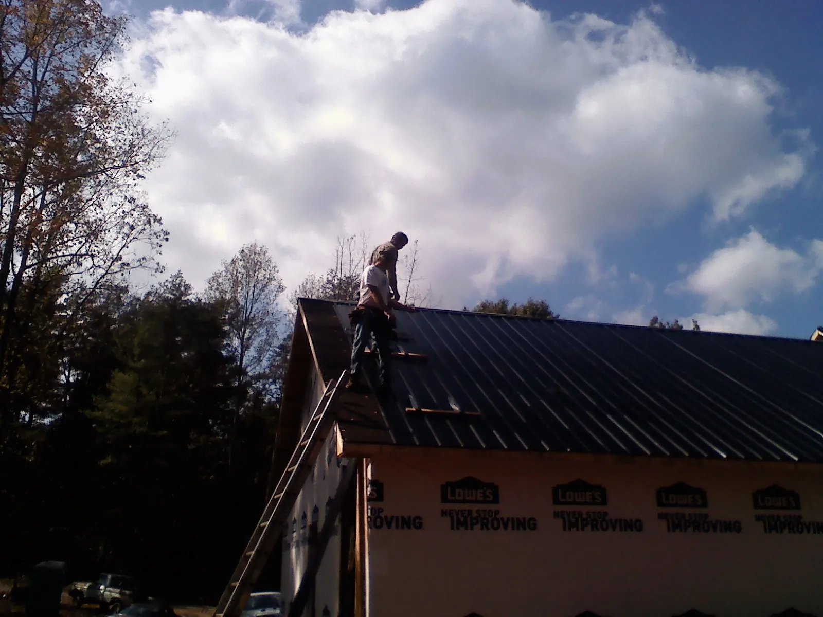 Roofer fastening dark metal panels high against a cloudy sky, from a Roof Inspection job in Hubbardsville