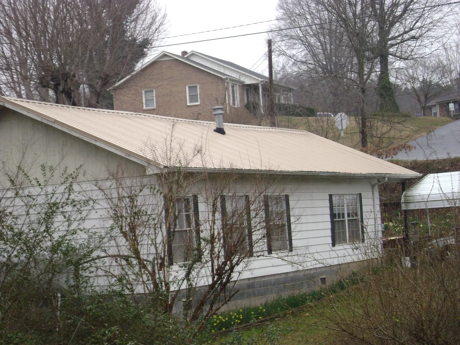 Tan metal roof on a white sided house set into a hillside — Commercial Roofing by Roofing Brothers in Hubbardsville